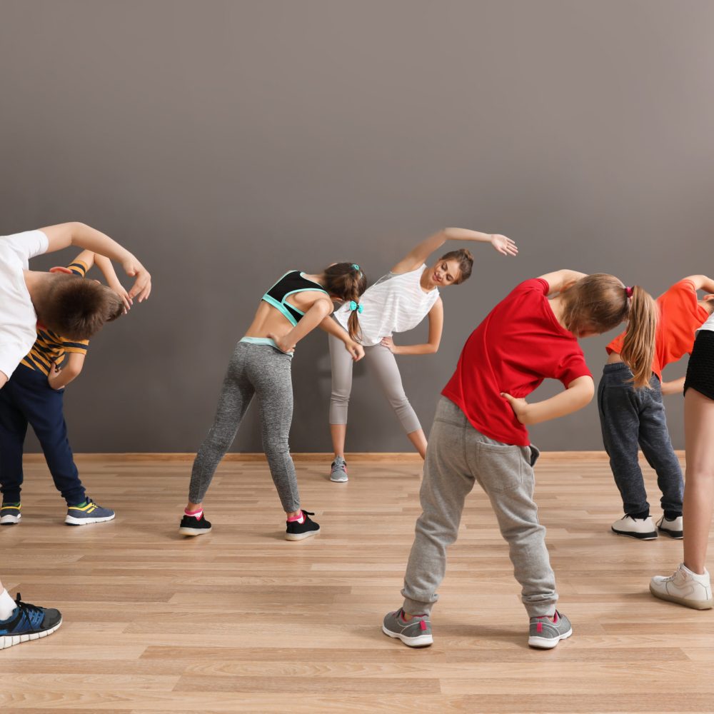 Cute little children and trainer doing physical exercise in school gym. Healthy lifestyle